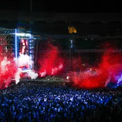 A sea of humanity united by music. We design our events to feel both immense and intimate, using powerful sound systems and immersive visuals like this red smoke effect to envelop the entire stadium in the performance.