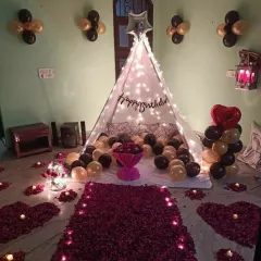 A complete birthday surprise package featuring a cabana tent, a rose petal pathway, and balloon decorations in black and gold for a sophisticated look.