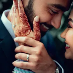 A close-up, intimate moment showing the bride's henna-adorned hand gently touching the groom's face.