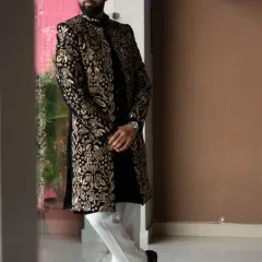 The groom looking regal in his full-length black and gold Indo-Western sherwani. This outfit perfectly balances traditional Indian artistry with a modern, structured silhouette.