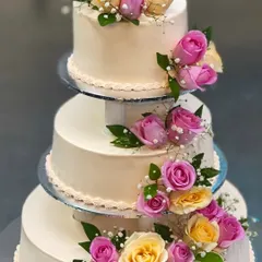 We believe your wedding cake should be as grand as your love story. This classic three-tiered cake, adorned with fresh pink and yellow roses, is a timeless centerpiece for any wedding celebration.