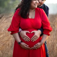 The classic heart-hands pose on the baby bump, set in a beautiful field during golden hour. This timeless shot is a sweet and direct expression of love for the little one on the way.