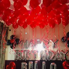 A classic birthday room setup using red and black balloons to cover the ceiling. The silver 'HAPPY BIRTHDAY' foil letters stand out and create a festive focal point in the room.
