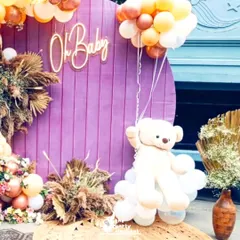 A close-up of the baby shower backdrop, showing the adorable teddy bear prop and the intricate balloon garland featuring pastel and rose gold balloons mixed with fresh flowers.