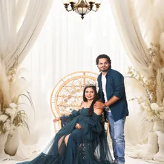 A regal studio portrait featuring an elegant chandelier and flowing drapes. The mother-to-be looks radiant in a dark teal gown, creating a sophisticated and classic maternity photo.