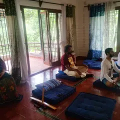 A group meditation at our retreat center, where individuals sit on cushions with a peaceful and focused demeanor. The natural light and tranquil surroundings provide the perfect setting for deep introspection and communion with the Divine.
