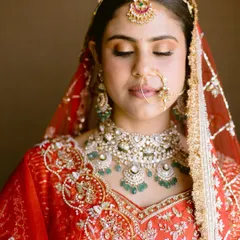A moment of quiet before the ceremony. This close-up showcases the soft, warm tones on her eyes, the perfectly blended skin, and the intricate details of her red bridal outfit and jewelry.