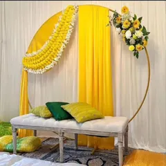 A modern ring backdrop for a Haldi or Mehendi ceremony. This design features a simple gold ring, draped yellow fabric, and a partial arch of marigold flowers, with a comfortable bench for seating.