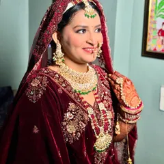 This bride is glowing in a deep maroon velvet lehenga. The makeup features a warm, radiant base and soft contouring to enhance her features for a regal wedding day look.