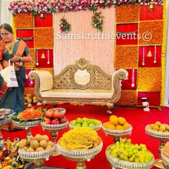 A simple yet elegant baby shower setup. The focus is on the beautiful arrangement of fresh fruits and sweets on silver stands, set against a traditional backdrop.