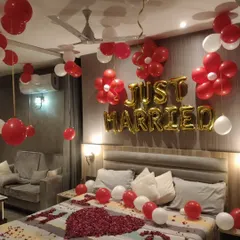 A beautiful first night room decoration in a hotel, featuring 'Just Married' foil balloons and flower-shaped balloon clusters. I used rose petals to create a heart on the bed, making it extra special for the couple.