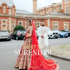 The bride stands in her magnificent red Rimple and Harpreet lehenga, its long train spread out, with the groom and the classic architecture of their London wedding venue creating a powerful, regal frame.