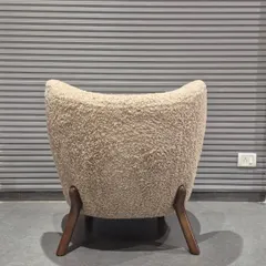 The back view of the bouclé accent chair, showing its curved, enveloping shape. This chair is perfect for a building lobby or a quiet reading corner.
