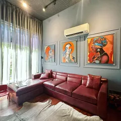 In this TV lounge, the design centers around a bold collection of wall art set against a cool-toned wall with neo-classical moulding. The rich, red leather sectional sofa adds a vibrant pop of color and luxurious comfort, while the animal hide rug introduces texture and a point of interest on the hardwood floor.