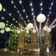 A beautiful terrace setup for a New Year's party, perfect for any evening celebration. The space is decorated with strings of fairy lights and hanging white paper lanterns, creating a warm and inviting atmosphere.