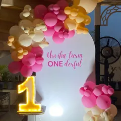 A simple and modern 'ONEderful' first birthday setup. The clean white backdrop is accented with a pink and orange balloon cluster and a bright, light-up number '1'.