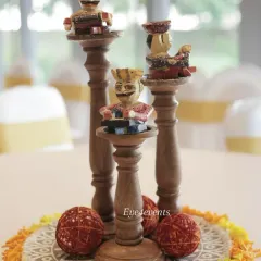 A close up of a unique table centerpiece inspired by Rajasthani culture. The decor features hand painted wooden figurines of traditional musicians placed on tiered wooden stands, surrounded by marigold petals.
