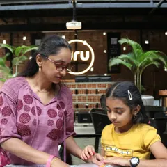 A mother and daughter work side-by-side on a flower pounding craft in an indoor workshop setting. This shows how our activities can be adapted for different locations, always focusing on the parent-child connection.