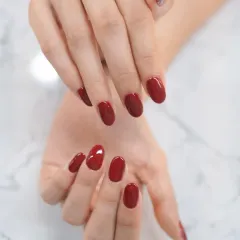 A sophisticated deep red gel polish on perfectly shaped short, natural nails for an elegant and understated look.