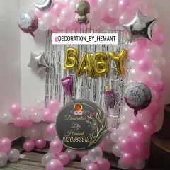 A sweet and simple baby girl welcome decoration. This setup features a balloon arch in pink and white against a silver fringe curtain, with "BABY" foil letters and other baby-themed foil balloons.