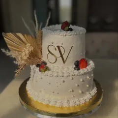 A classic two-tiered engagement cake with the couple's initials. The design is kept clean and elegant with dried pampas grass, fresh berries, and simple piping.