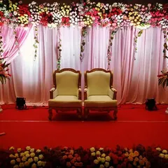 A classic and elegant stage for a formal ceremony. This setup features two ornate chairs for the guests of honor, set against a backdrop of soft pink drapes and a lush floral border.