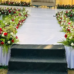 The stage aisle for an outdoor event, lined with continuous arrangements of red and white roses, leading up to the main seating area.