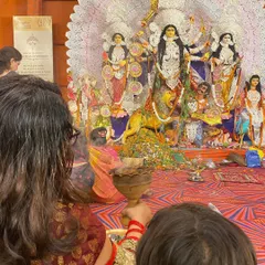 An over the shoulder view showing a devotee's perspective during the Dhunuchi Naach, with the magnificent Durga idol in the background.
