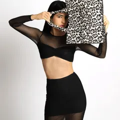 A bold and playful accessory shot. The model is styled in a sheer black top and skirt, creating a minimalist canvas to highlight the statement leopard-print tote bag.