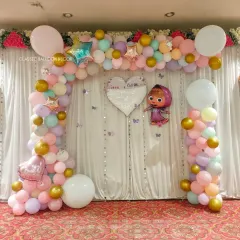 This naming ceremony backdrop features a Masha and the Bear theme. A pastel balloon arch frames a white curtain backdrop with a custom heart-shaped sign.