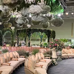A wide view of the Italian garden reception, showcasing the circular seating arrangement, the floating floral clouds on the ceiling, and the central mandap, all unified by a palette of green and pastel florals.