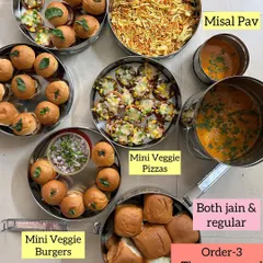A hi-tea spread featuring Mini Veggie Pizzas, Mini Veggie Burgers, and a deconstructed Misal Pav, with both Jain and regular options available.
