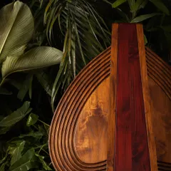 A detail shot of the Vismayam chair's backrest, where layers of wood are carved to ripple like the folds of a Theyyam costume. The central band of rich, red-toned wood is a direct nod to the fiery colors used in the art form.