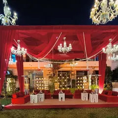 A breathtaking outdoor Sangeet setup with a stage draped in rich red fabric and illuminated by dozens of crystal chandeliers.