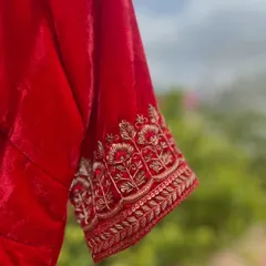 A close-up of the intricate zardosi embroidery on the sleeve cuff of the bright red velvet blouse.
