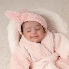 A one-month-old enjoying her first spa day. This adorable setup with the pink robe and bunny ears is one of my most popular creative themes.