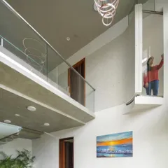 The double-height living space is the heart of the home, visually connecting the two floors. The curved balcony and glass-encased lift add a sculptural, modern element to the interior.