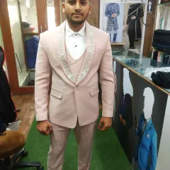 This client is seen during a fitting for his three-piece suit in a distinctive light pink fabric. The design includes detailed embroidery on the waistcoat and lapels, showcasing our ability to create unique, personalized groomswear.