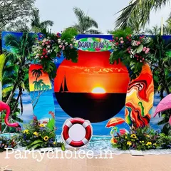 A close-up of the vibrant, tropical backdrop. The design includes a central sunset graphic, surfboard cutouts, and floral arrangements, creating a perfect photo opportunity for guests.