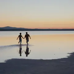 A silhouette of a couple running joyfully through the water at sunset in Turkey. This image is full of life and freedom, capturing a moment of pure, uninhibited happiness.