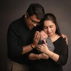 A classic newborn family portrait against a simple dark backdrop. This style puts all the focus on the emotional connection and the peacefulness of your sleeping baby.