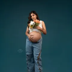 A modern and edgy maternity portrait of a mom-to-be in ripped jeans and a crop top, holding a bouquet of flowers.