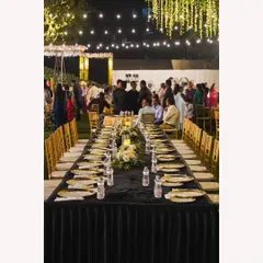An intimate long-table setup for a special sit-down dinner under the stars. The black tablecloth, golden plates, and ambient lighting create a sophisticated and memorable dining experience.