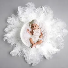 A creative overhead shot of a baby in a white knitted outfit, surrounded by a circle of soft white feathers. This creates a beautiful, angelic look.