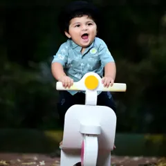 A happy baby boy enjoying a ride on his toy scooter in a park setting.
