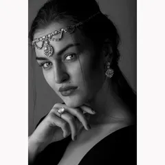 An intense black and white portrait for a jewellery campaign. The focus is on the model's direct gaze and the exquisite detail of the traditional headpiece and ring, captured with classic lighting to create a timeless and powerful image.