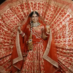 A smiling bride in a traditional red lehenga. The detailed gota patti work and matching jewelry set are available for rent.