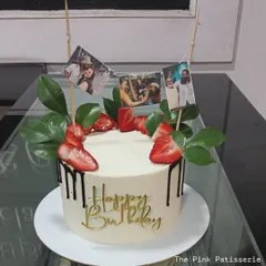 A unique way to display memories. This birthday cake is decorated with a mini banner of personal photos, fresh strawberries, and a chocolate drip.