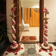 The entrance to a home decorated for a house warming ceremony, featuring deepams wrapped in beautiful pink and white floral garlands.