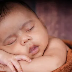 A beautiful close-up shot focusing on the baby's peaceful face, with their hands tucked under their cheek in a classic newborn pose.